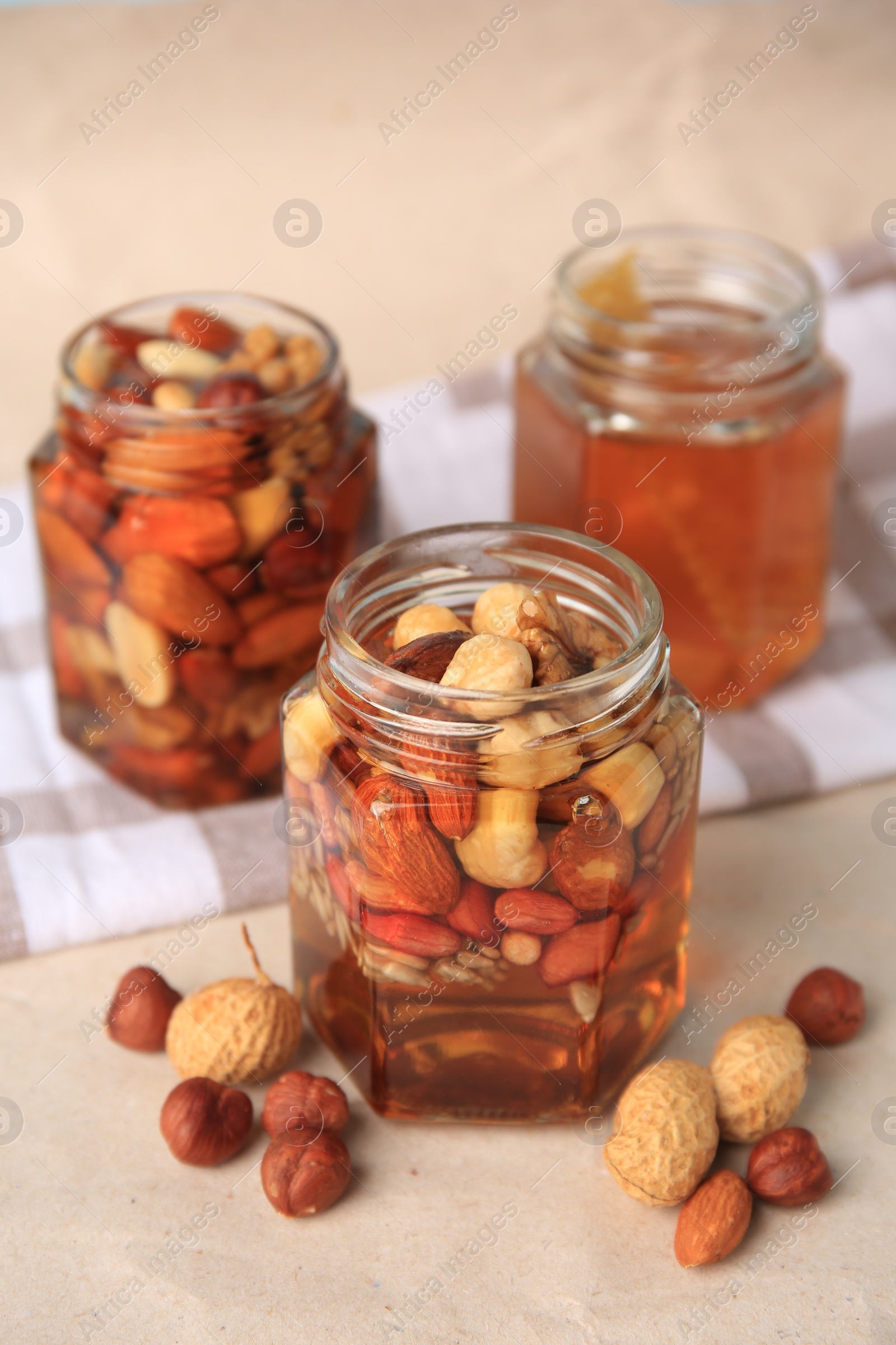 Photo of Jars with different nuts and honey on beige table