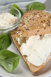 Photo of Pieces of bread with cream cheese and basil leaves on plate, closeup