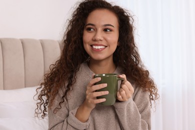 Photo of Happy African American woman with cup of drink in bedroom