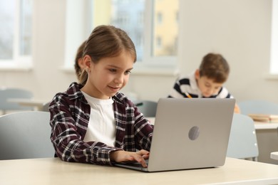 Photo of Cute little girl with laptop studying in classroom at school