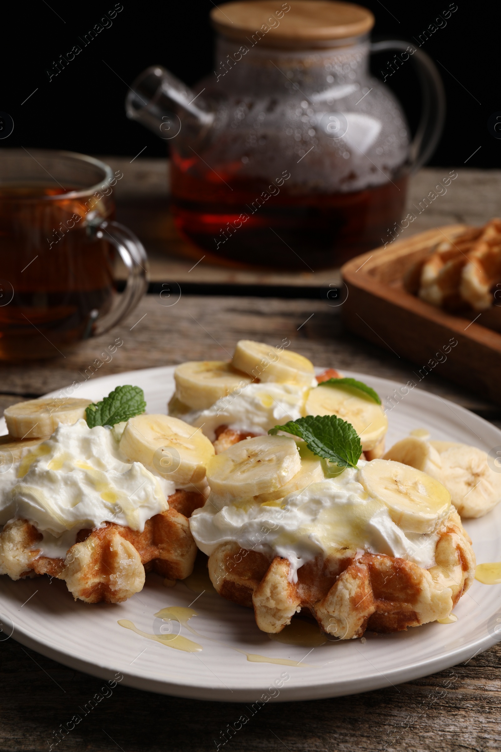 Photo of Delicious Belgian waffles with banana and whipped cream served on wooden table
