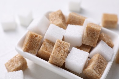 Photo of Different sugar cubes in bowl on white table, closeup