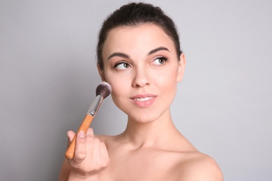 Photo of Young woman applying makeup on grey background. Professional cosmetic products