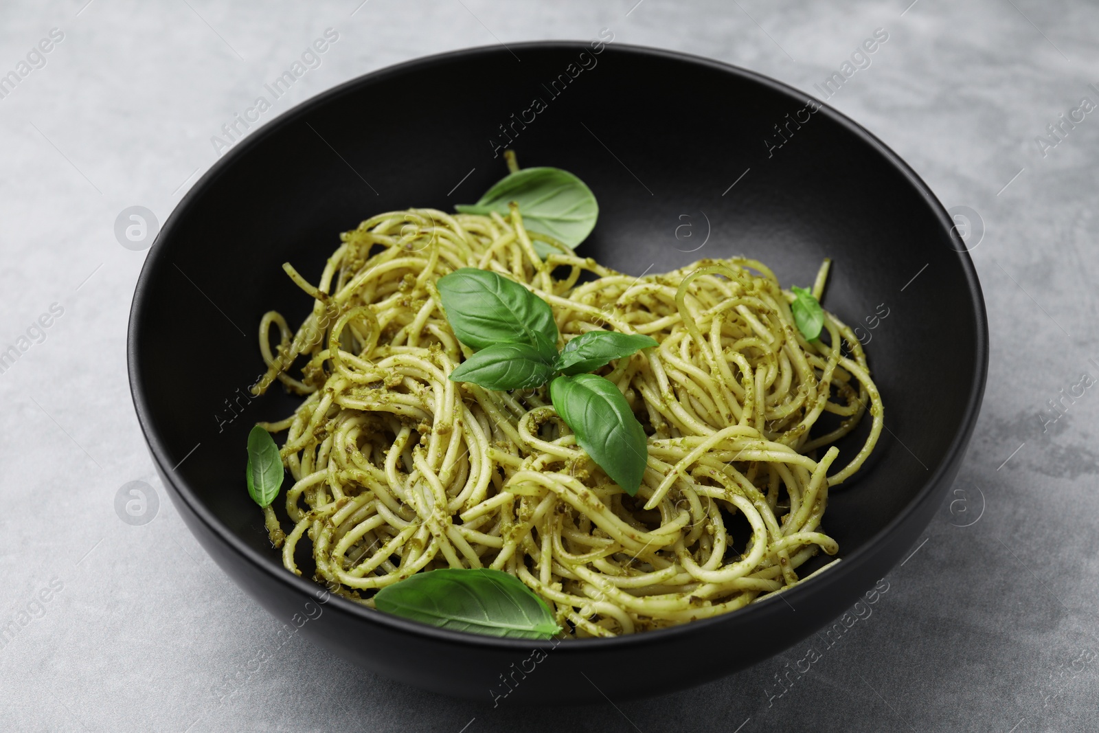 Photo of Delicious pasta with pesto sauce and basil on light grey table, closeup