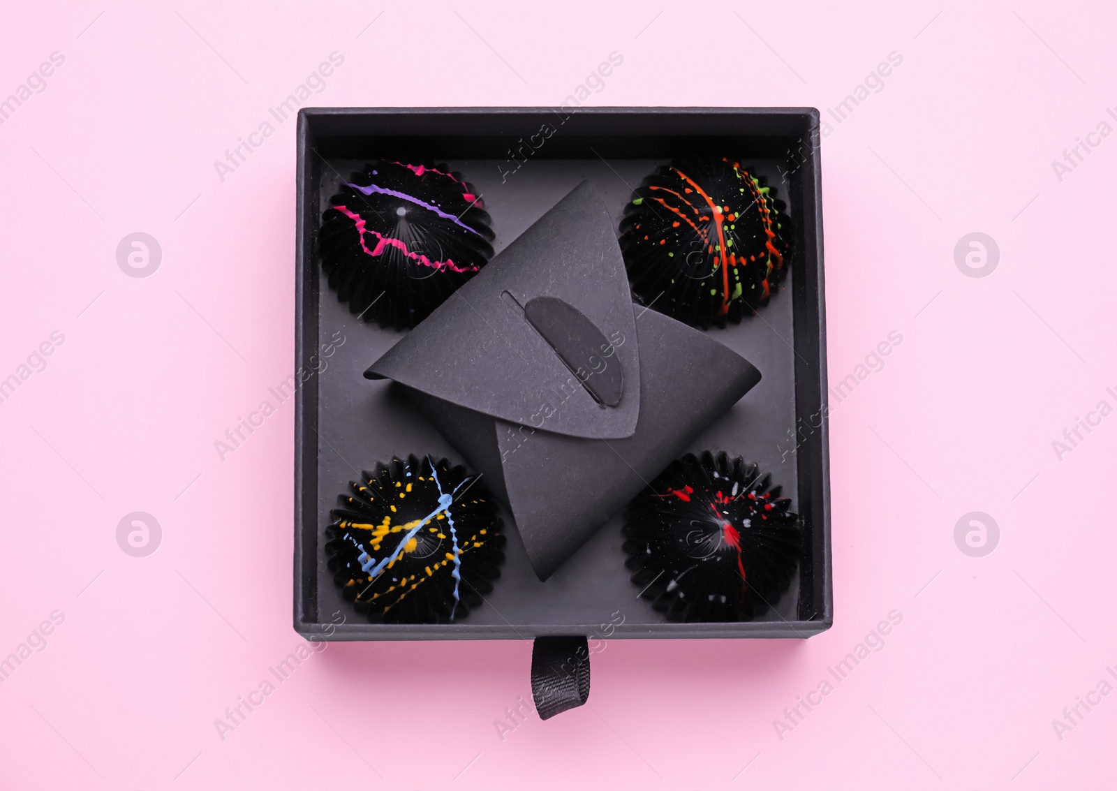 Photo of Box of tasty chocolate candies on pink background, top view