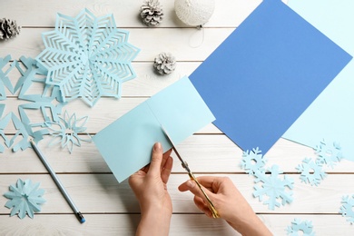 Photo of Woman making paper snowflake at white wooden table, top view
