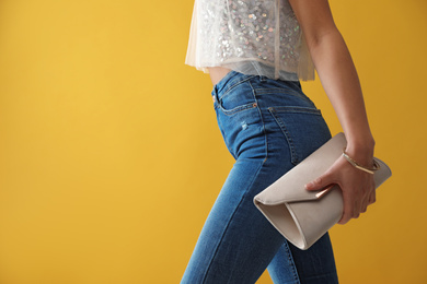 Photo of Woman in jeans with clutch purse on yellow background, closeup. Space for text