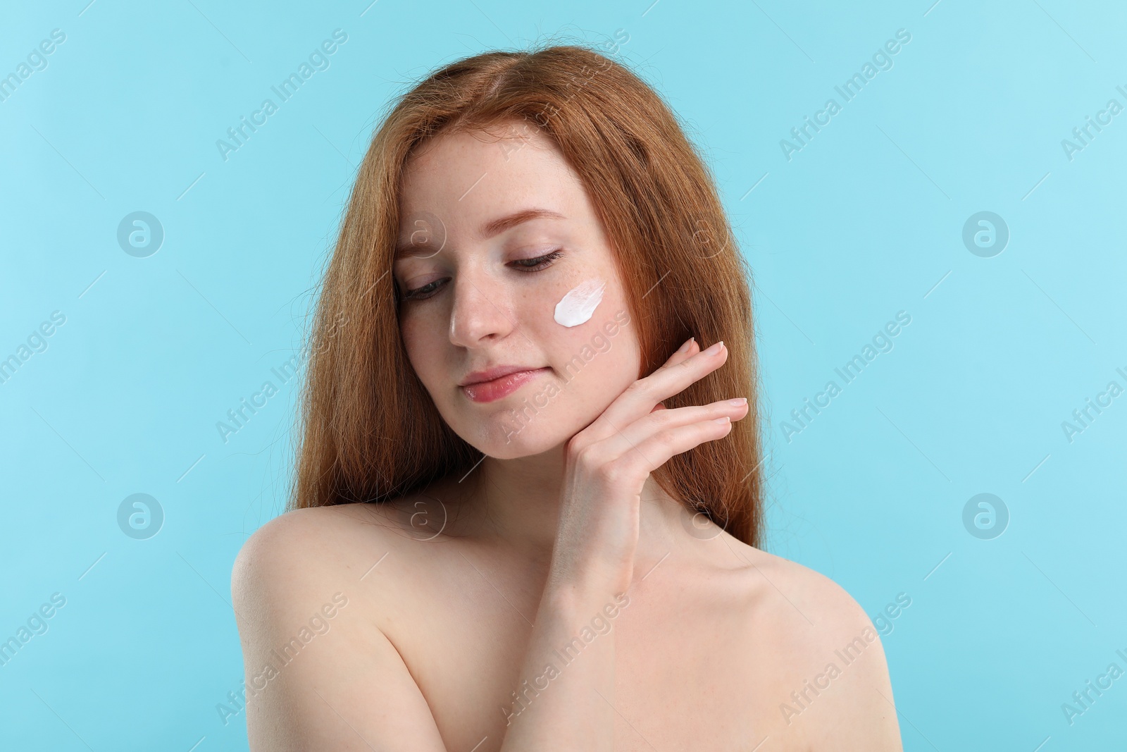 Photo of Beautiful woman with freckles and cream on her face against light blue background