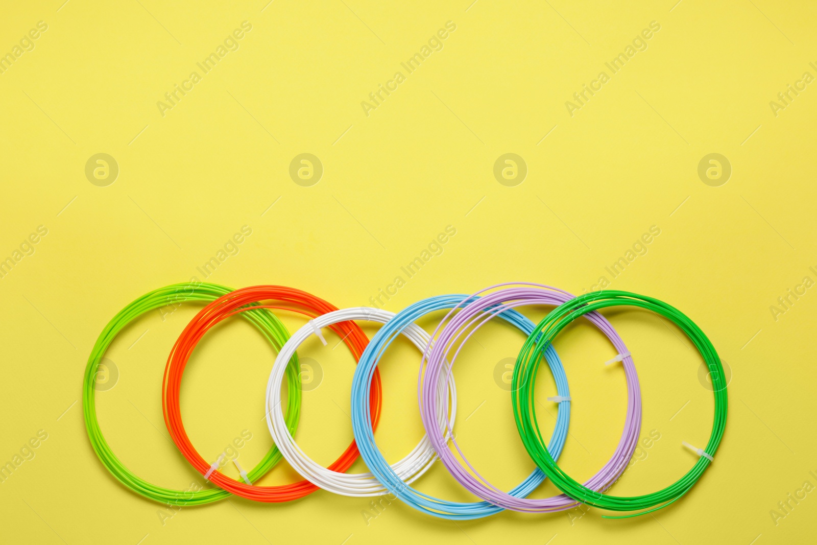 Photo of Colorful plastic filaments for 3D pen on yellow background, flat lay. Space for text