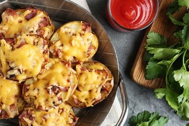 Flat lay composition with pan of baked potatoes, sauce and parsley on grey background