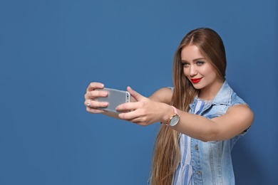 Attractive young woman taking selfie on color background