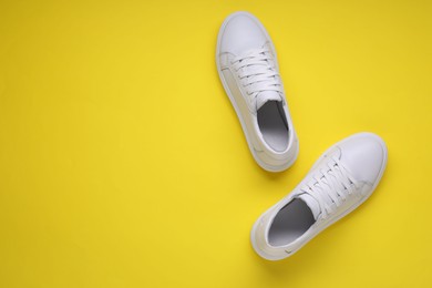 Photo of Pair of stylish white sneakers on yellow background, top view. Space for text