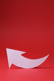 Photo of White curved paper arrow on red background, space for text