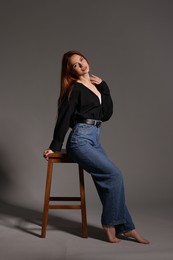 Beautiful young woman sitting on stool against gray background