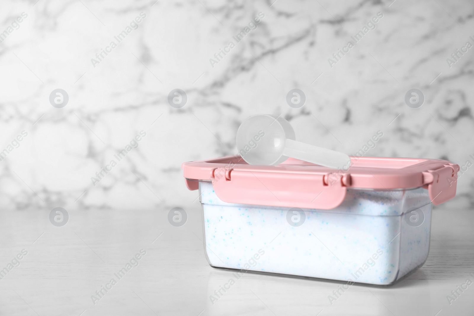 Photo of Closed container with detergent powder and measuring spoon on table. Space for text