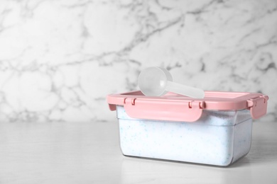 Photo of Closed container with detergent powder and measuring spoon on table. Space for text