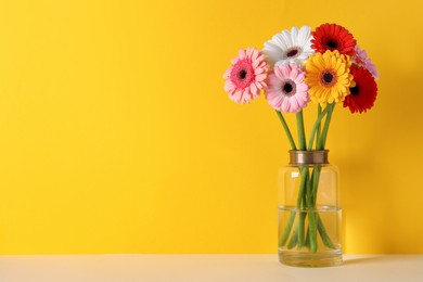 Photo of Bouquet of beautiful colorful gerbera flowers in vase on table against yellow background. Space for text