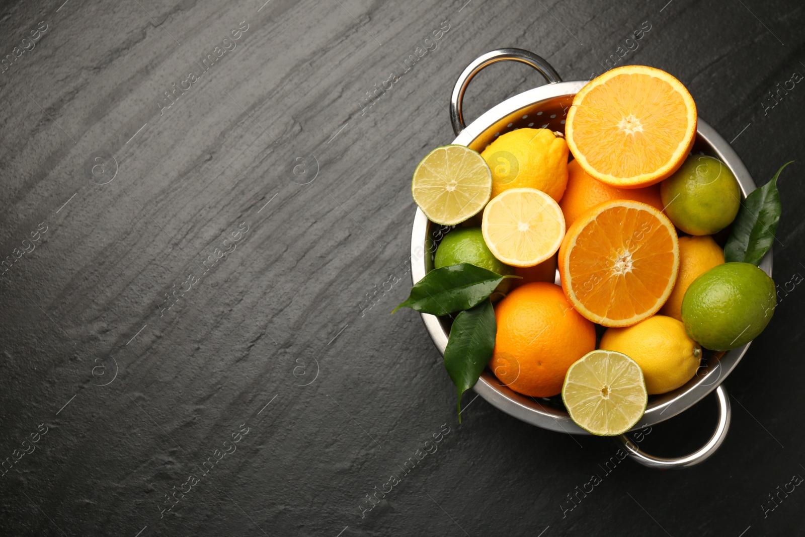 Photo of Fresh citrus fruits in colander on dark textured table, top view. Space for text