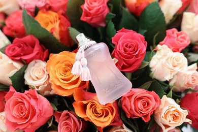 Photo of Bottle of perfume on bouquet of beautiful roses, top view