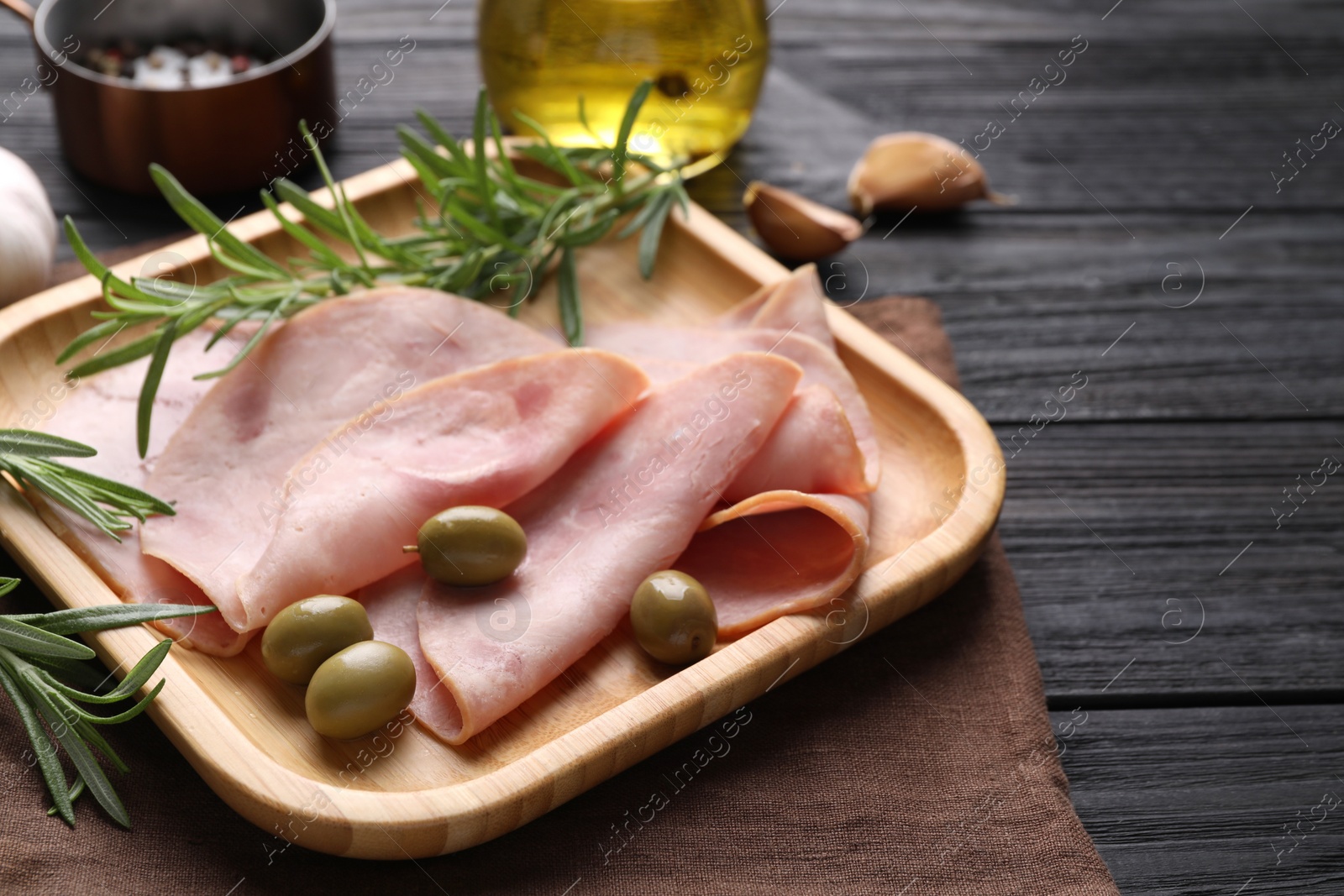 Photo of Slices of delicious ham with rosemary and olives served on dark wooden table. Space for text