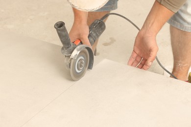 Photo of Worker cutting tiles with circular saw indoors, closeup