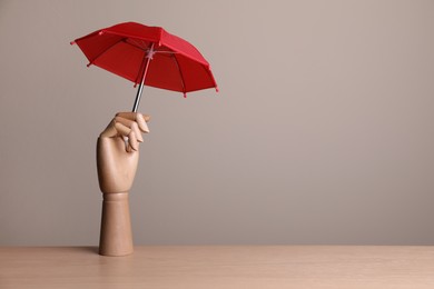 Photo of Small umbrella in mannequin's hand on wooden table. Space for text