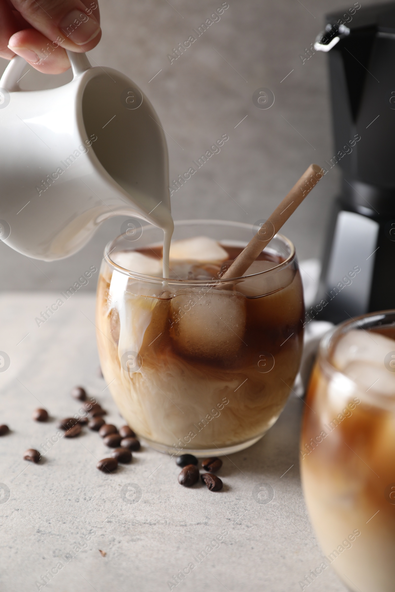 Photo of Woman pouring milk into glass with refreshing iced coffee at gray table, closeup