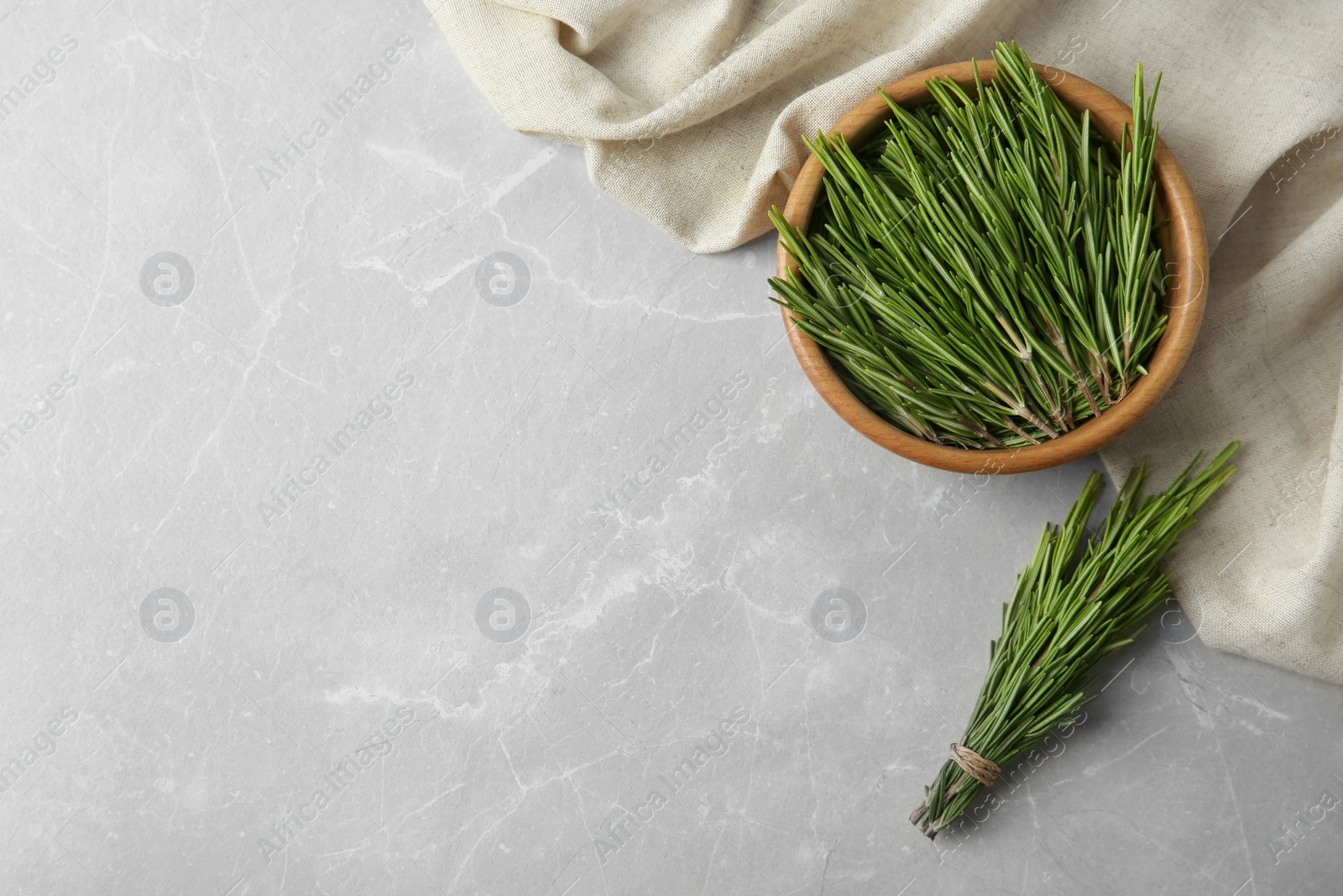 Photo of Bowl with fresh rosemary twigs on grey marble background, flat lay. Space for text