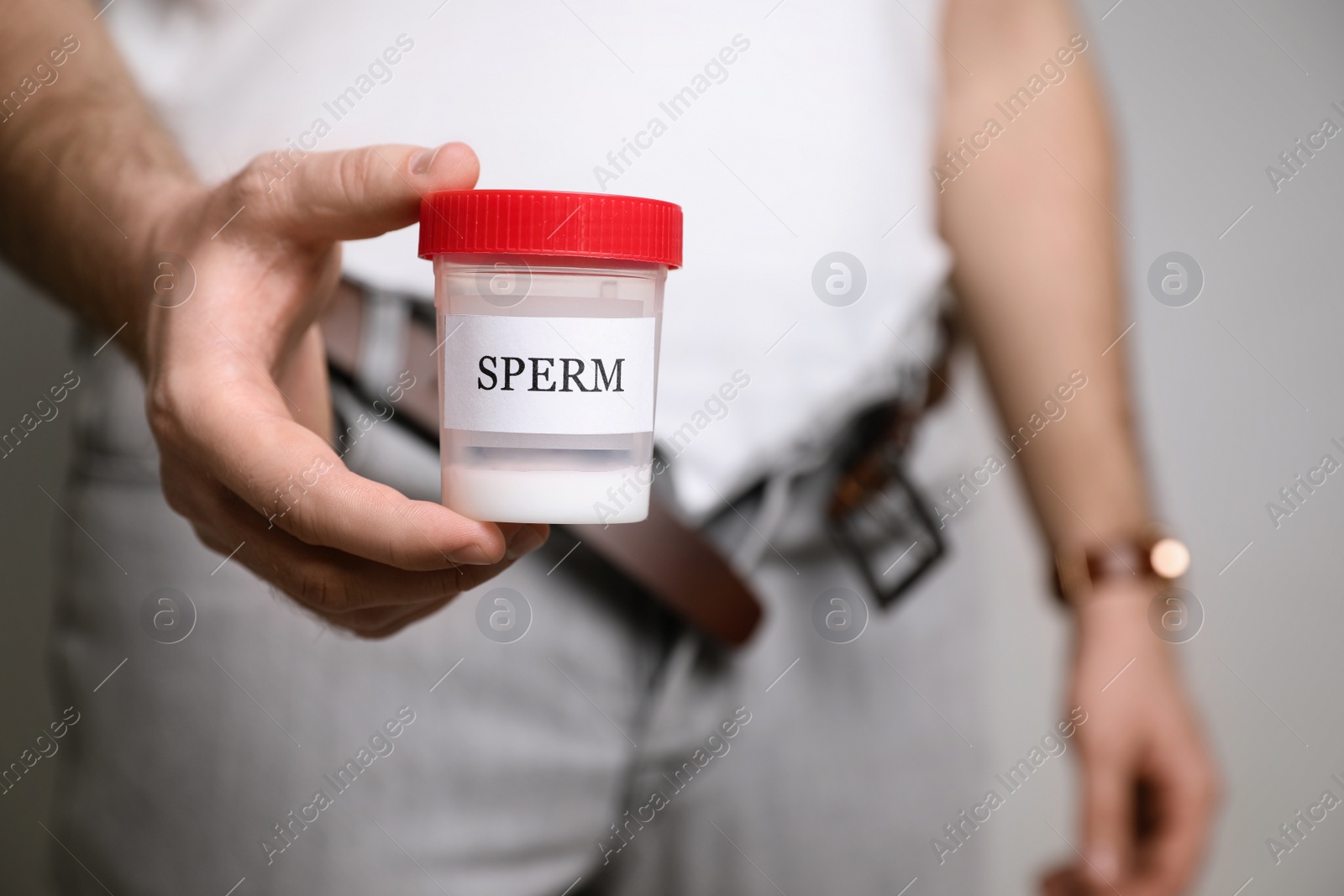 Photo of Donor with unzipped pants holding container of sperm, closeup