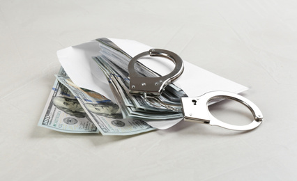 Dollar bills and handcuffs on light grey stone table. Bribe concept