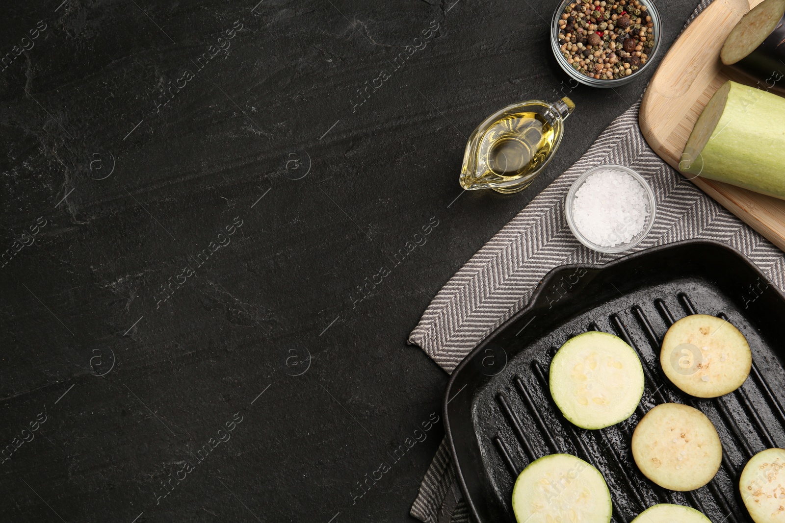 Photo of Grill pan with slices of zucchini on black table, flat lay. Space for text