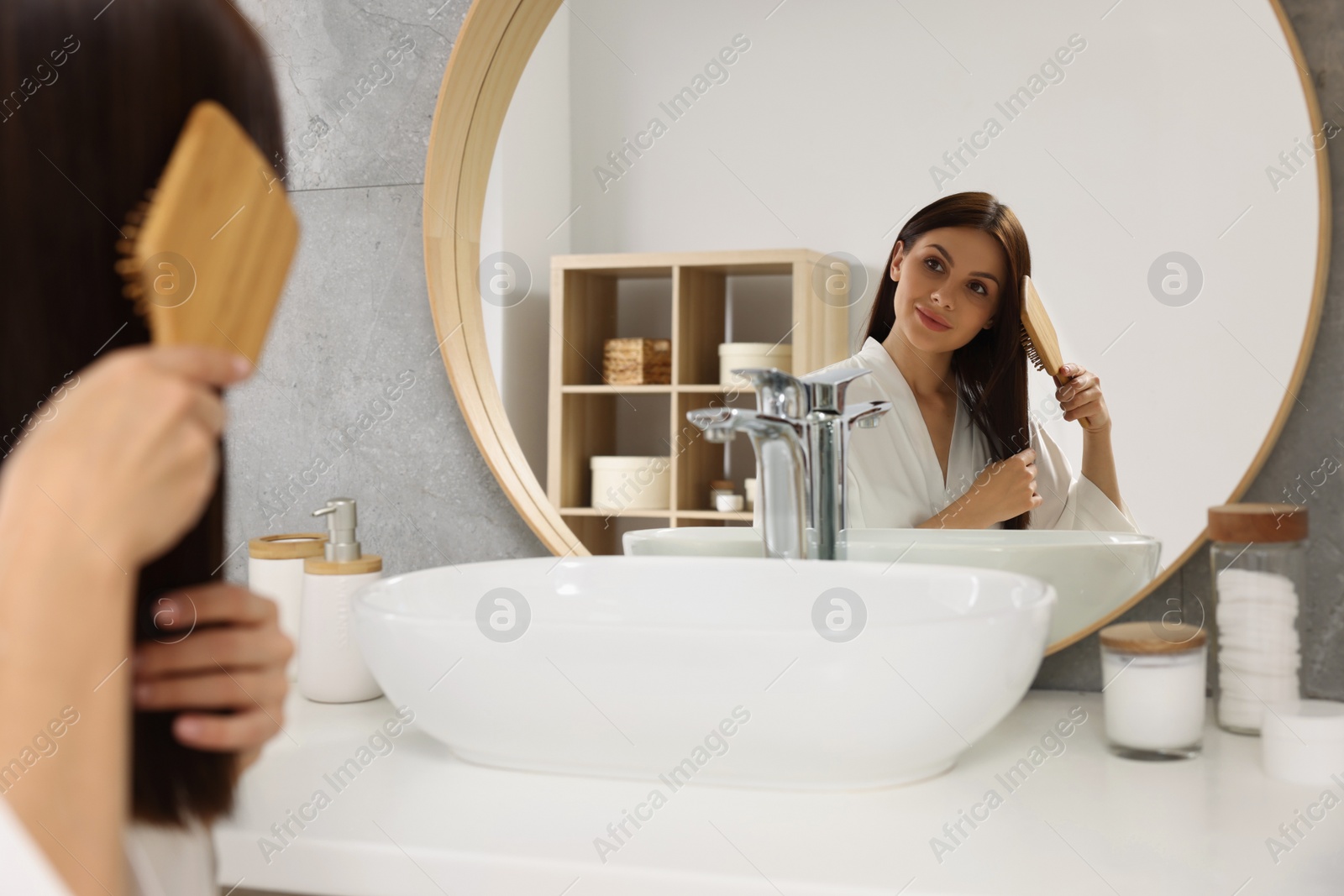 Photo of Beautiful woman brushing her hair near mirror in bathroom