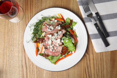 Photo of Delicious salad with roasted meat and vegetables served on wooden table, flat lay