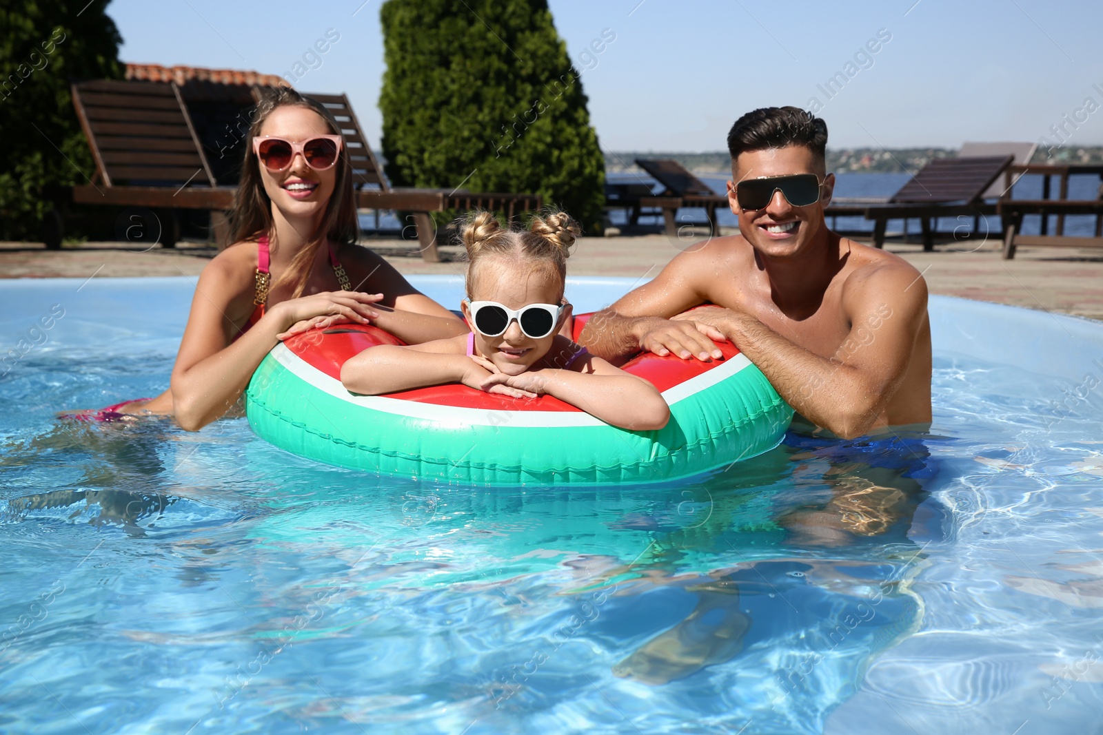 Photo of Happy family with inflatable ring in outdoor swimming pool on sunny summer day