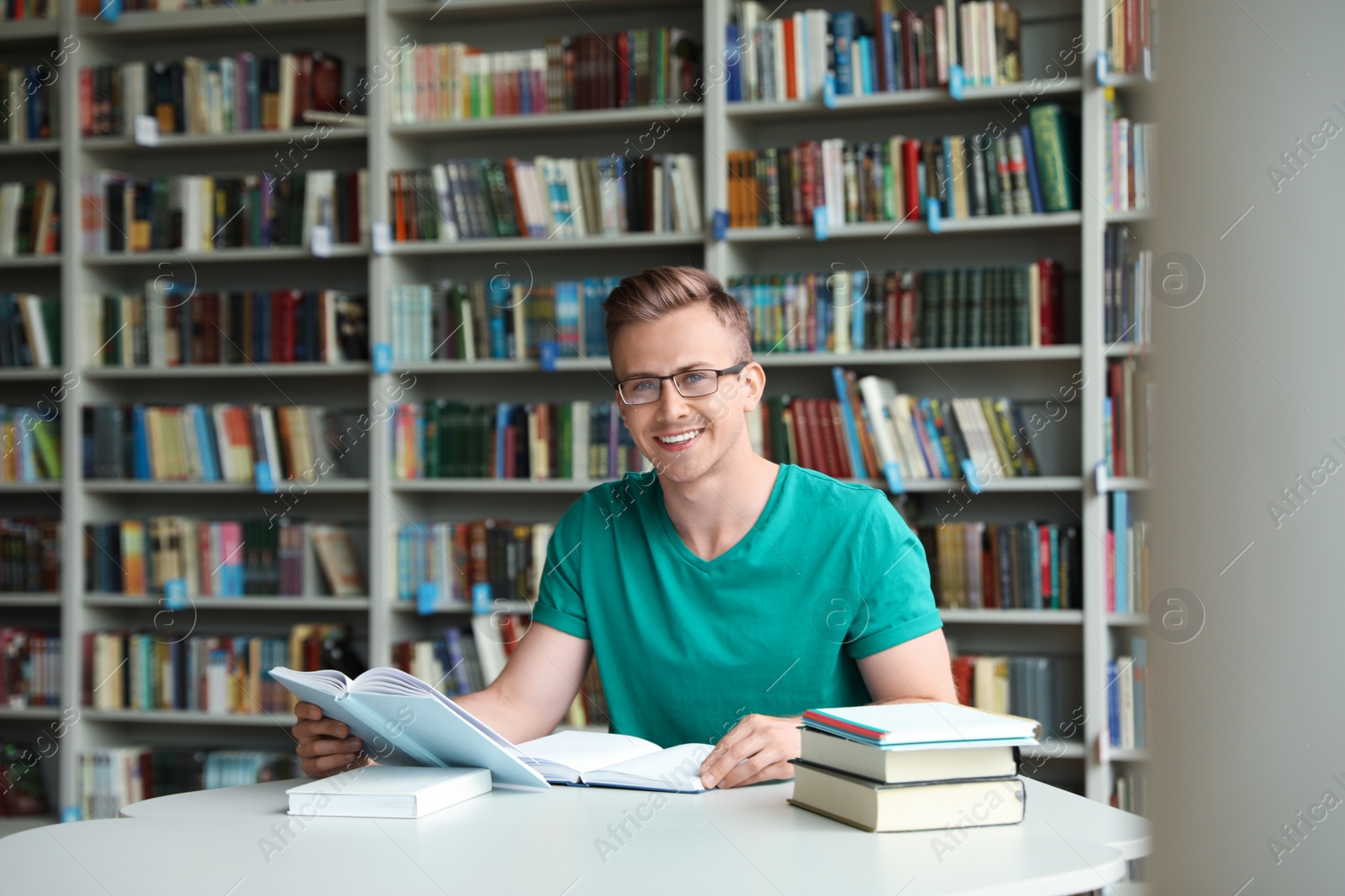 Photo of Young man with books at table in library