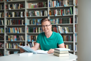 Young man with books at table in library