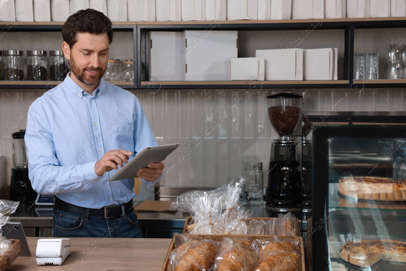 Photo of Smiling business owner with tablet at cashier desk in bakery shop