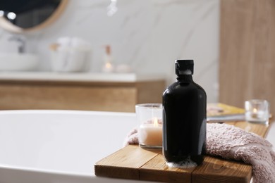 Photo of Wooden bath tray with shower gel, candle and fresh towel on tub indoors. Space for text