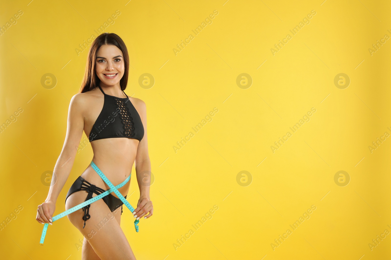 Photo of Attractive young woman with slim body measuring her waist on color background. Space for text