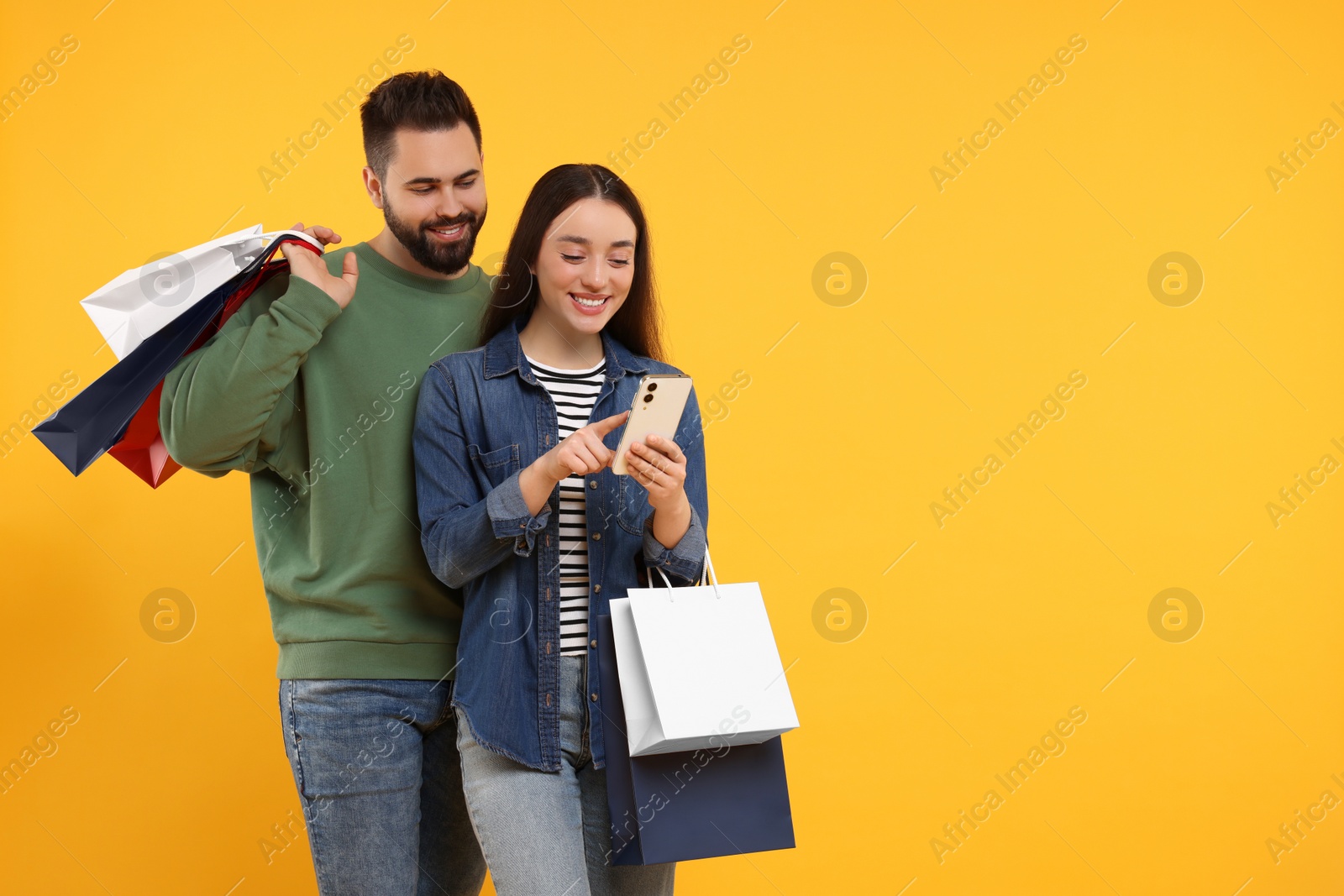 Photo of Happy couple with shopping bags and smartphone on orange background. Space for text