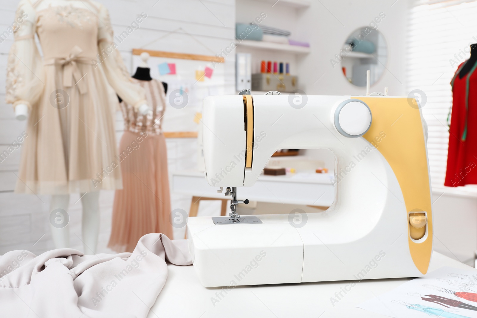 Photo of Modern sewing machine, fabric and accessories on table in dressmaking workshop