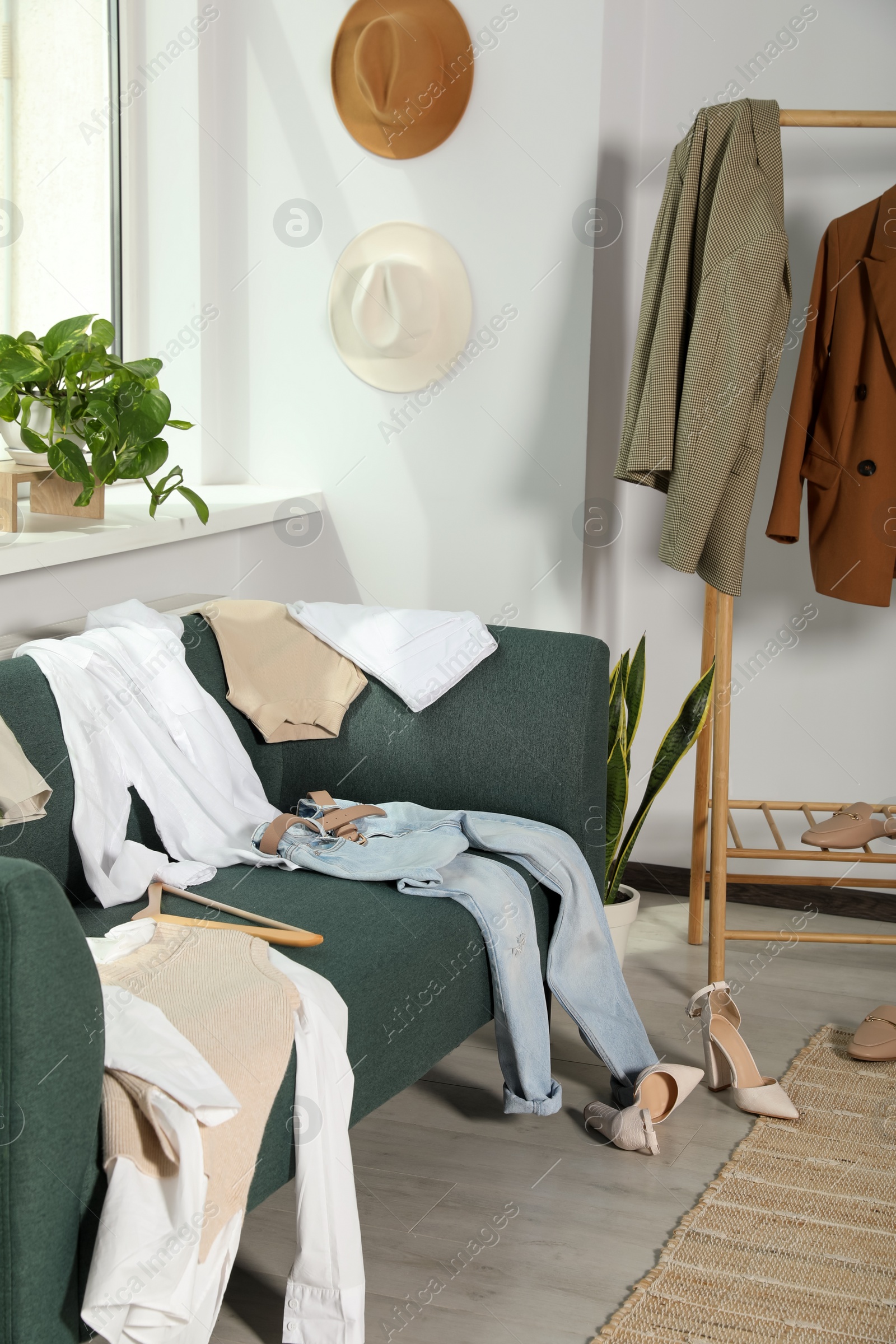 Photo of Messy pile of clothes on sofa and shoes in living room