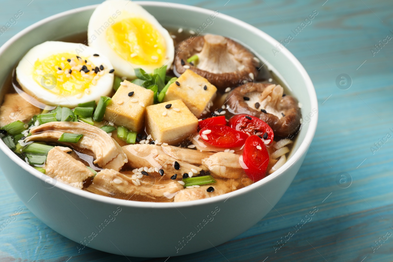 Photo of Bowl of delicious ramen on light blue wooden table. Noodle soup