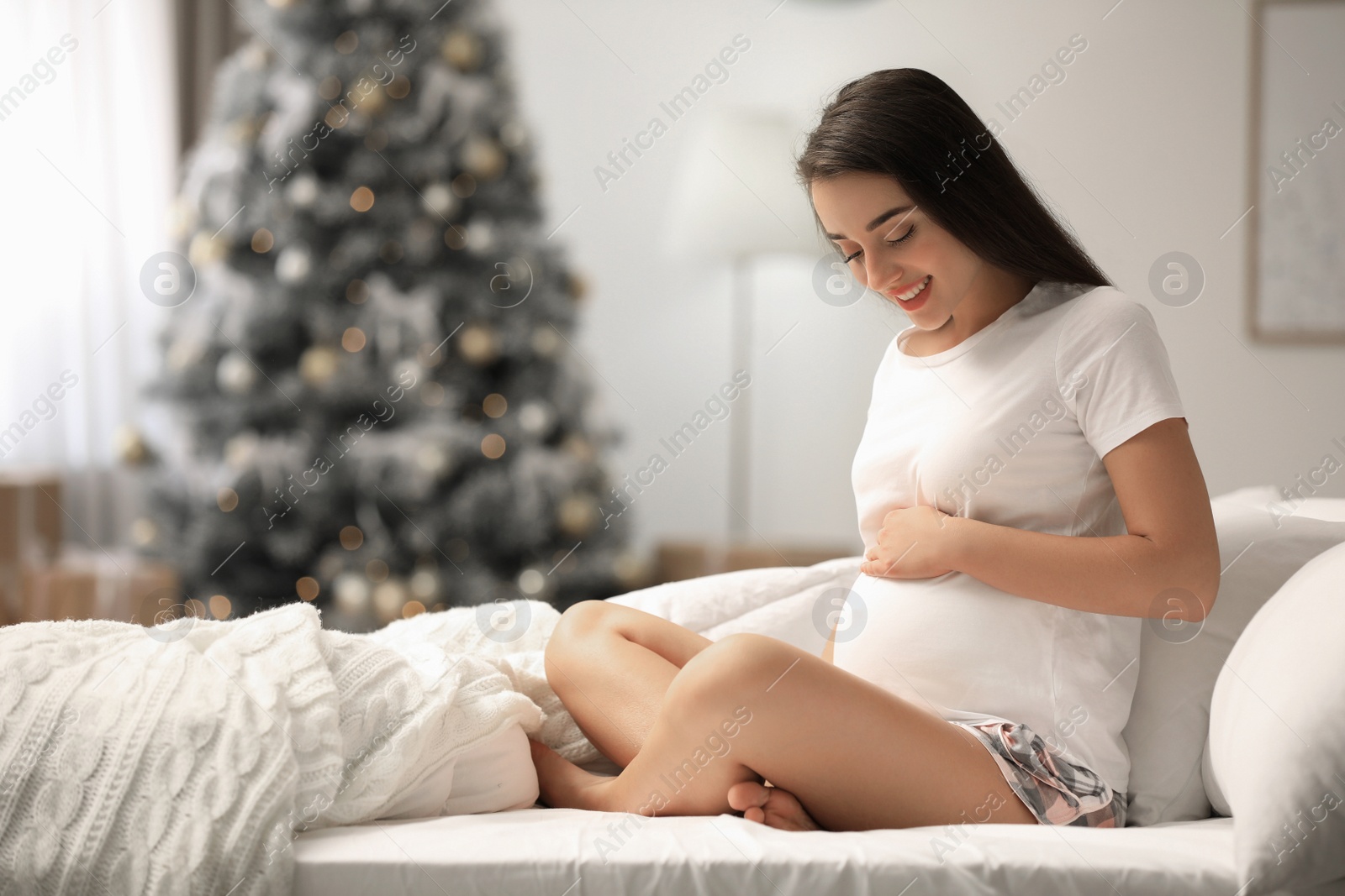 Photo of Happy pregnant woman on bed in room decorated for Christmas. Expecting baby