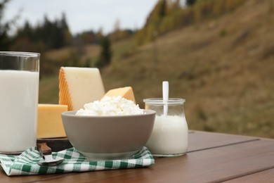 Photo of Tasty cottage cheese and other fresh dairy products on wooden table outdoors