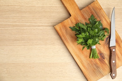 Board with fresh green parsley and knife on wooden background, top view. Space for text