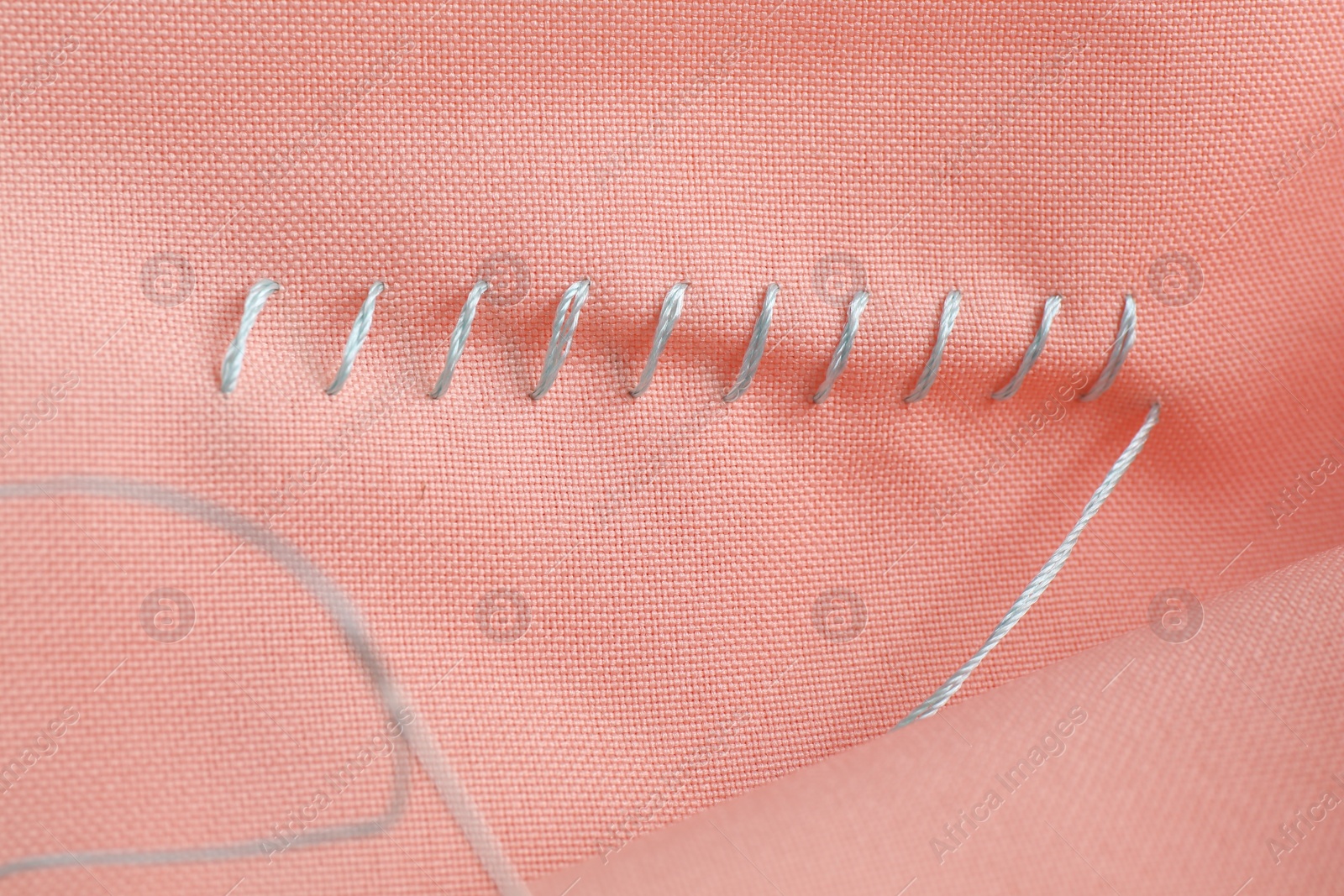 Photo of Sewing thread and stitches on coral cloth, top view