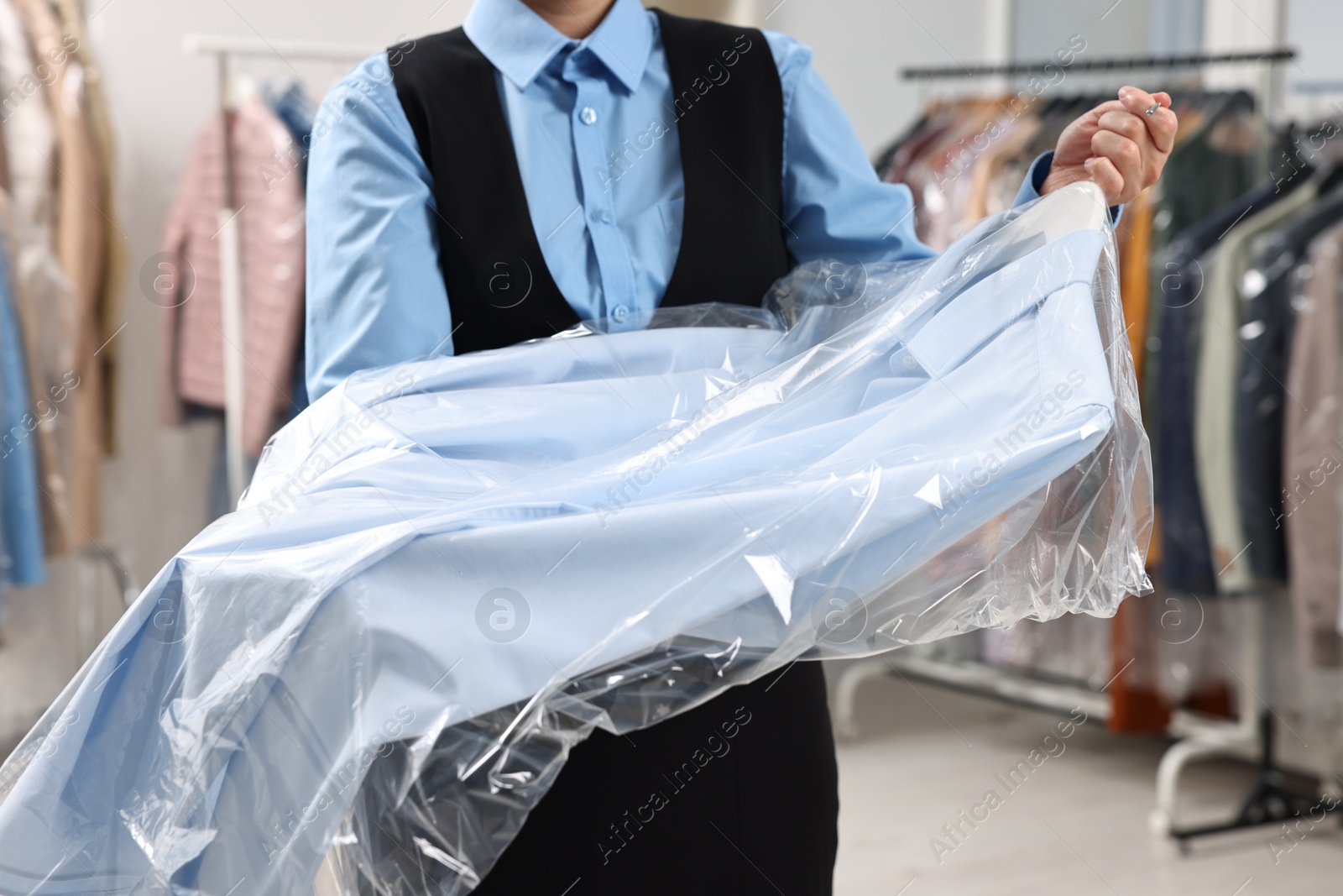 Photo of Dry-cleaning service. Woman holding shirt in plastic bag indoors, closeup