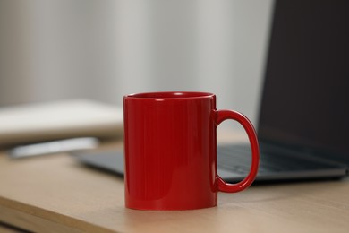 Red ceramic mug and laptop on wooden table at workplace