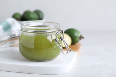 Photo of Feijoa jam in glass jar on light grey table, closeup. Space for text